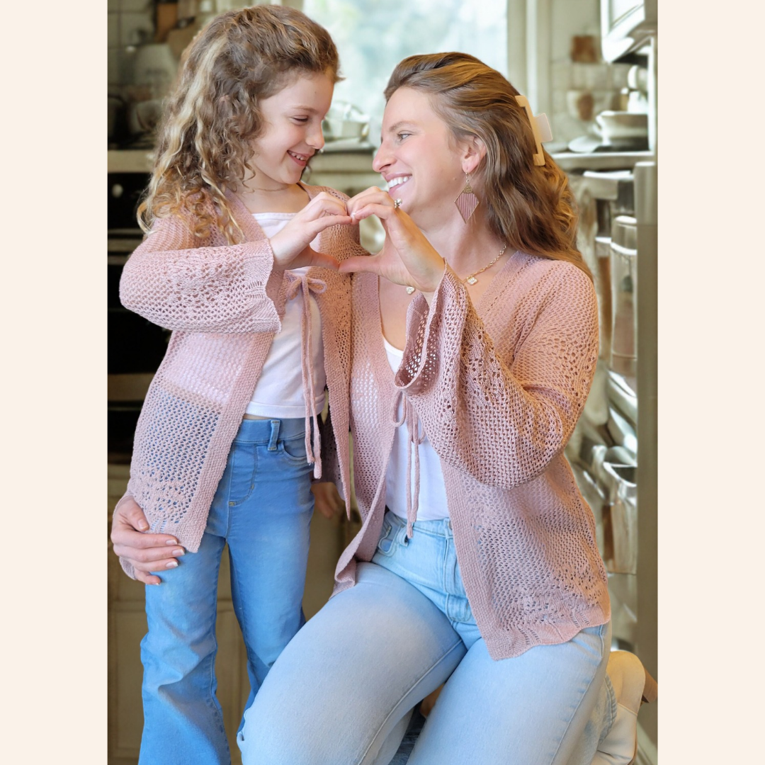 Woman and young girl wearing matching pink crochet cardigans in a kitchen setting