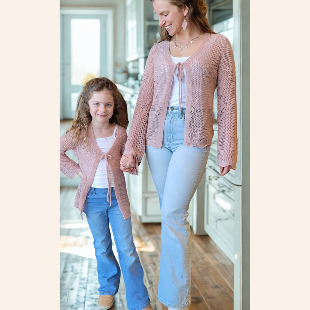 Woman and young girl wearing matching pink cardigans in a kitchen.