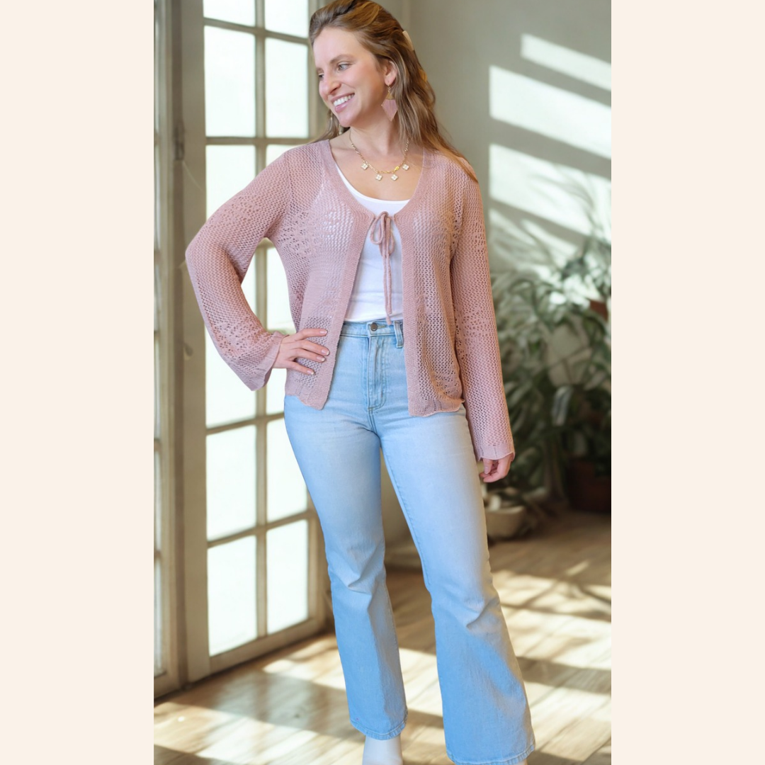 Woman wearing a pink cardigan and light blue jeans standing in a well-lit room.