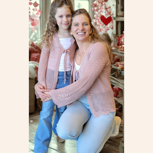Woman and young girl wearing matching pink cardigans in a decorated room.