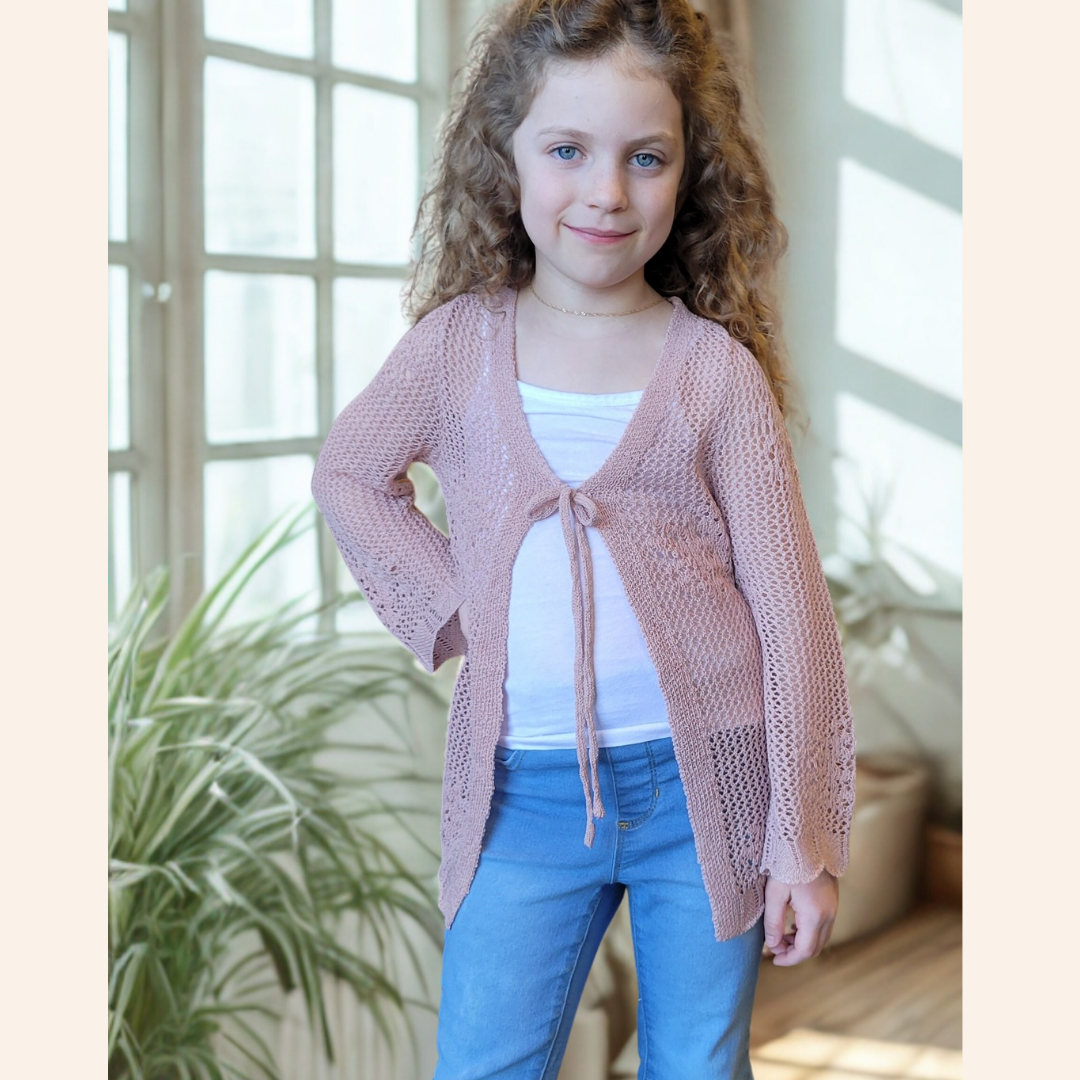 Young girl wearing a pink knitted cardigan and blue jeans indoors.