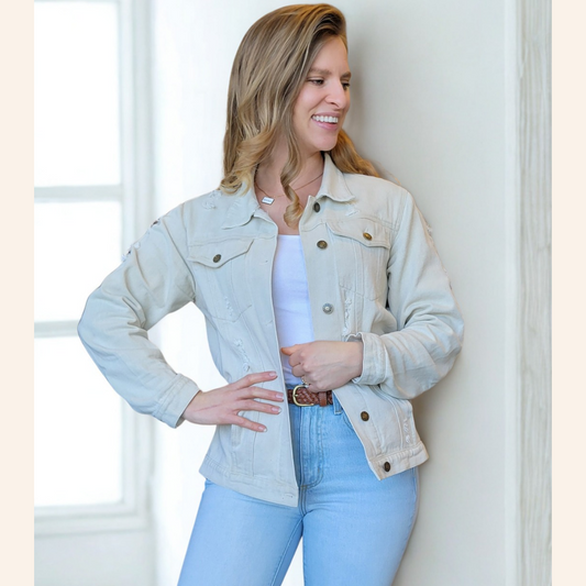 Woman wearing a light blue denim jacket and jeans standing against a white wall.