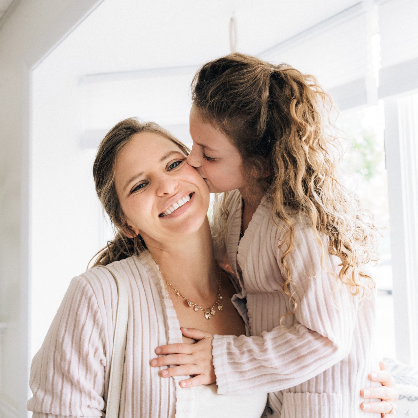 Woman and young girl in matching outfits standing close together indoors.