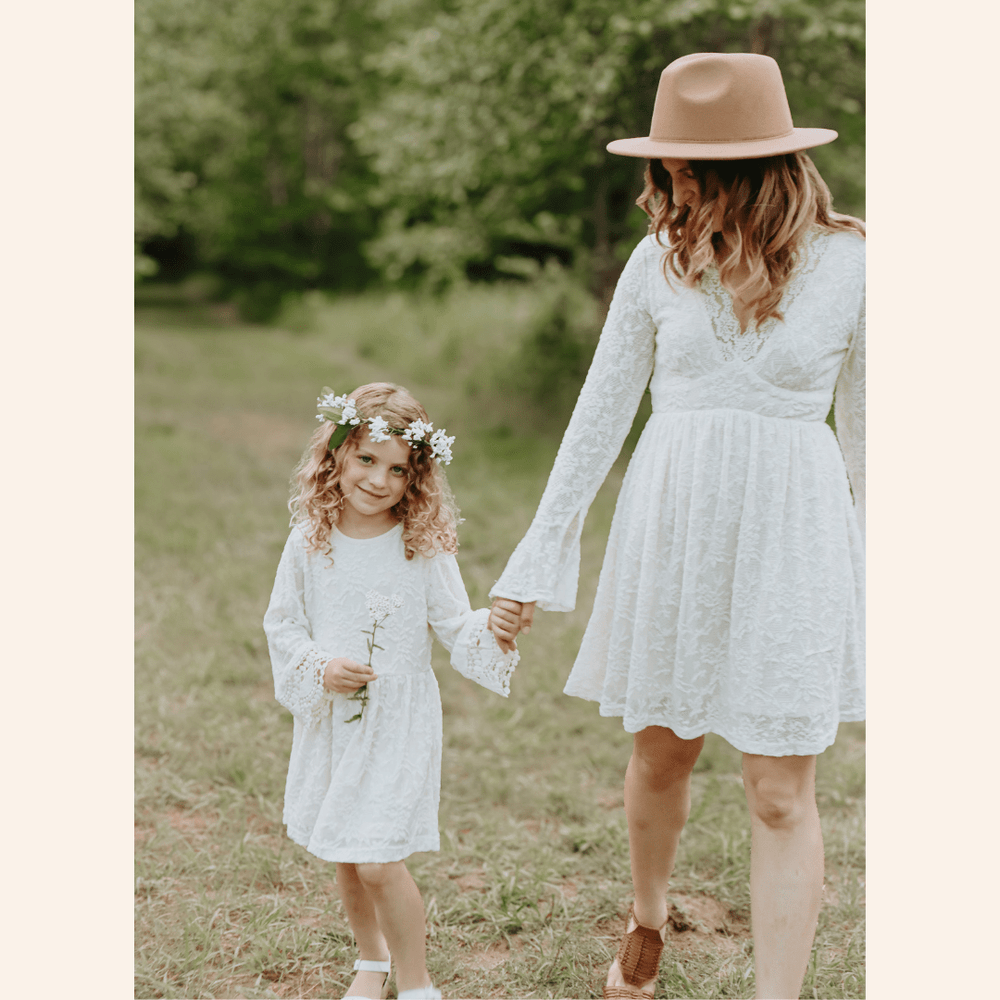 Woman and child in white dresses holding hands in a grassy field