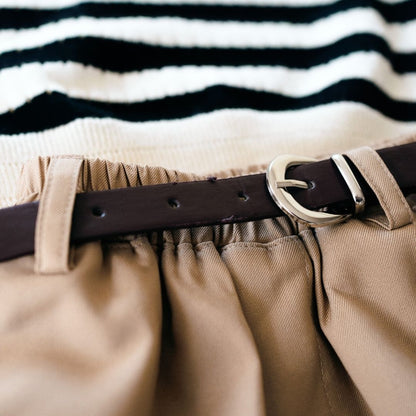 Close-up of beige pants with a brown belt and striped shirt in the background