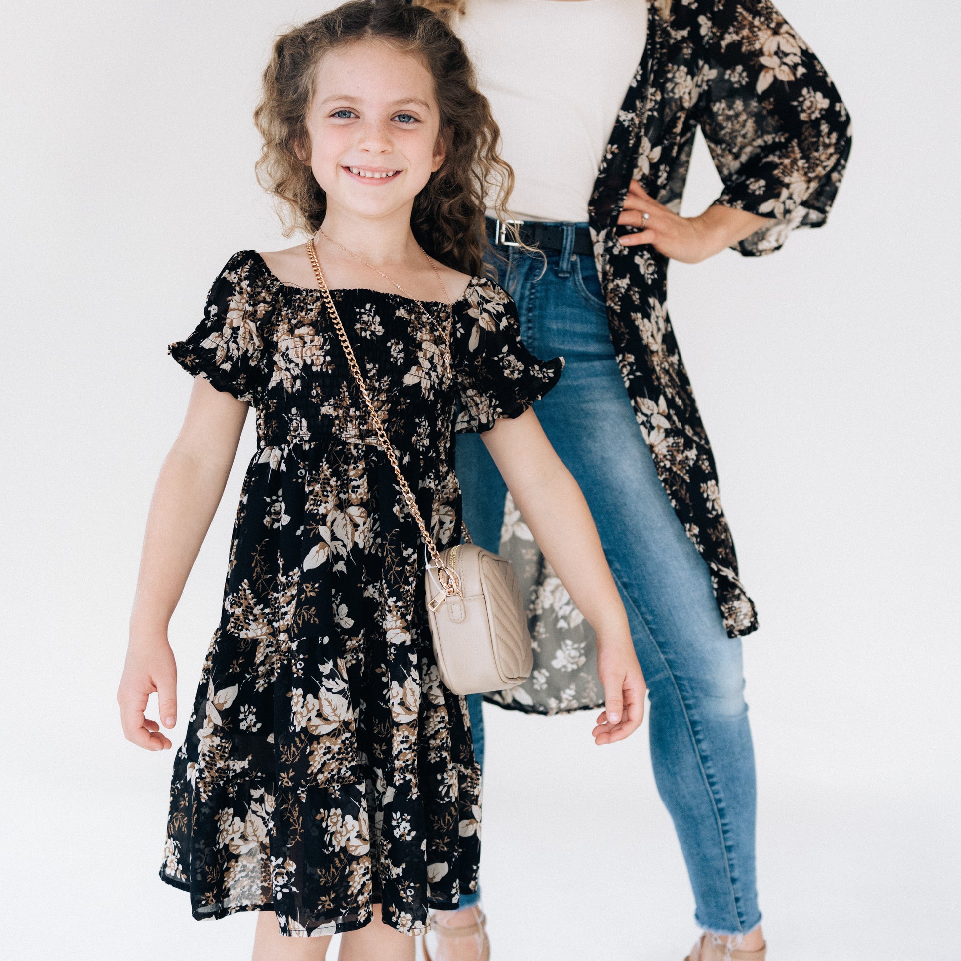 Young girl wearing a black floral dress standing next to an adult wearing a floral kimono and jeans.