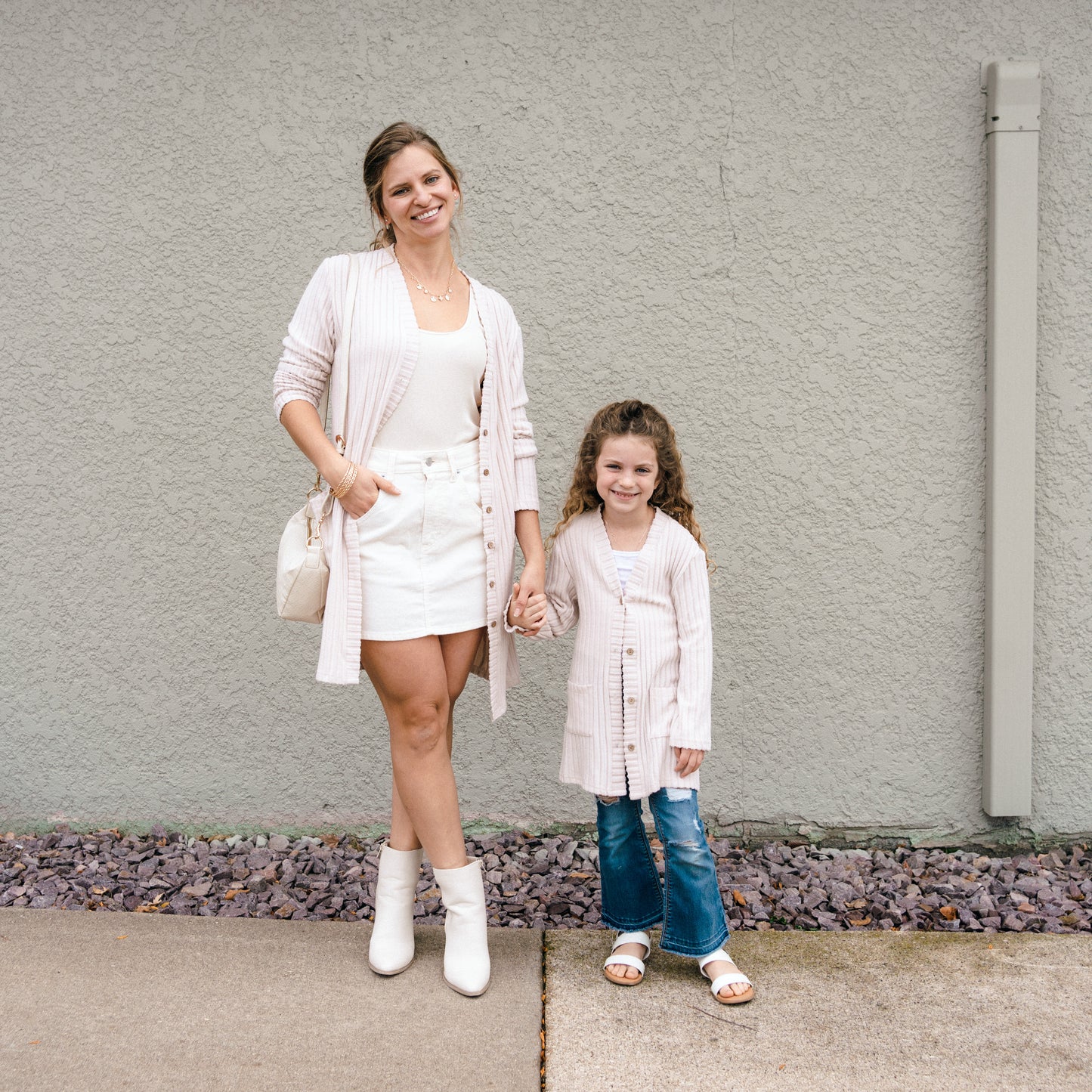 Woman and young girl holding hands in front of a gray wall