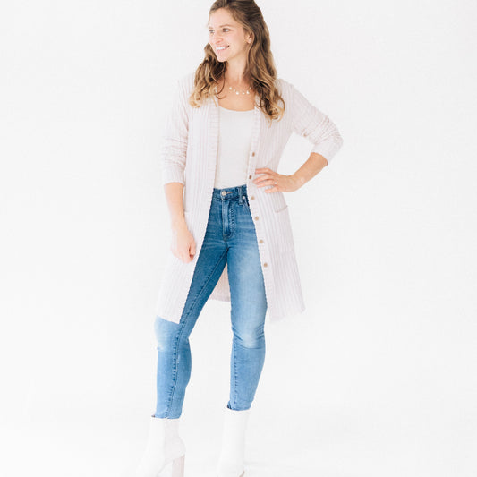 Woman wearing a long white cardigan, white shirt, and blue jeans on a white background